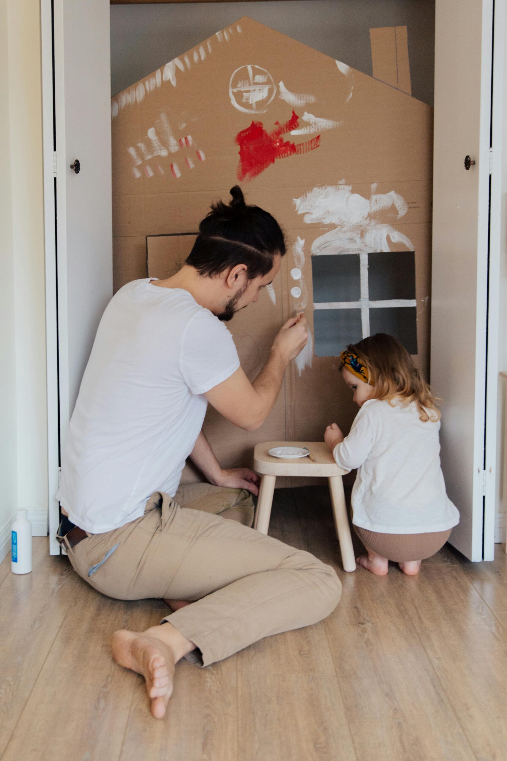 pexels-photo-3933227-3933227 Father and daughter painting a cardboard house indoors, enjoying quality time together.